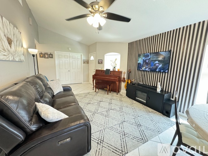 A living room with a black leather couch and a ceiling fan.