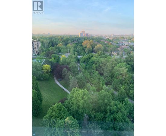 A lush green park with a winding path and apartment buildings in the background.
