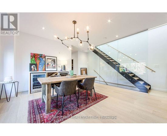 A dining room with a wooden table and chairs, a chandelier, and a staircase in the background.