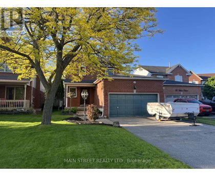 A tree with yellow leaves stands in front of a brick house.