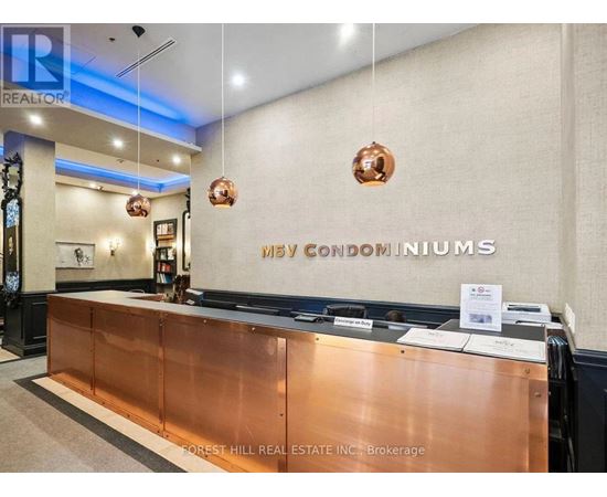 The lobby of a building with a copper reception desk and a sign that reads "May Condominiums.".
