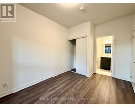 A room with wooden flooring and white walls, with a doorway leading to another room.
