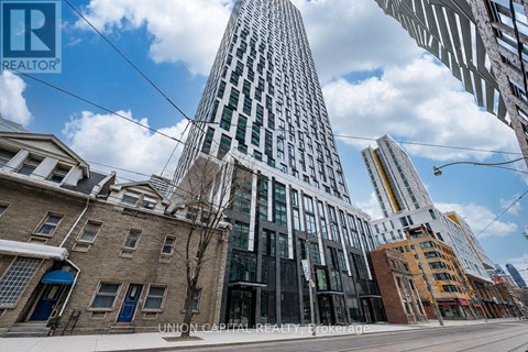 A tall building with a glass facade stands in the middle of a city street.