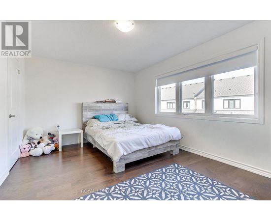 A bedroom with a bed, a teddy bear, a nightstand, a rug, and a window.