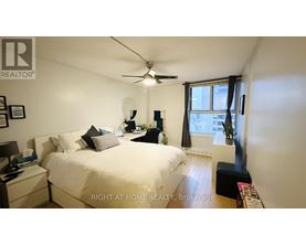 A bedroom with a bed, nightstand, and a window with a view of the city.