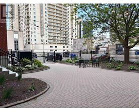 A brick patio with a tree and chairs in front of apartment buildings.