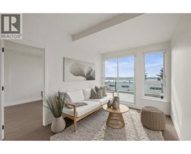 A living room with a white couch, a wooden coffee table, and a large window with a view of the water.