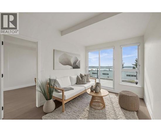A living room with a white couch, a wooden coffee table, and a large window with a view of the water.