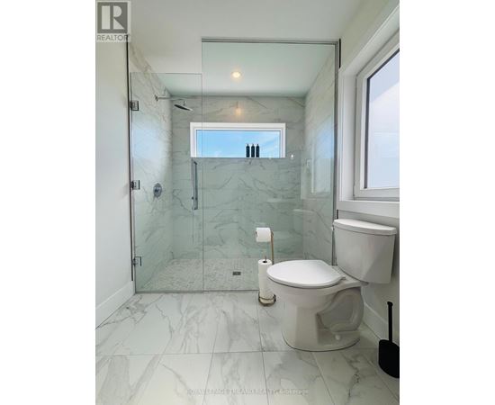 A white toilet in a marble bathroom with a glass shower door.