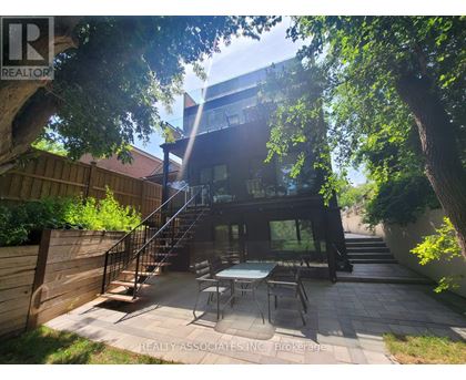 A patio with a table and chairs is surrounded by trees and a wooden fence.