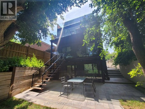 A patio with a table and chairs is surrounded by trees and a wooden fence.