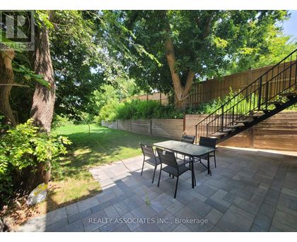 A patio with a table and chairs is surrounded by greenery.