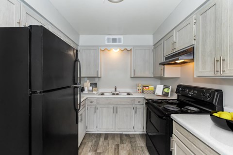 A black refrigerator stands in a kitchen with wooden floors and white cabinets.