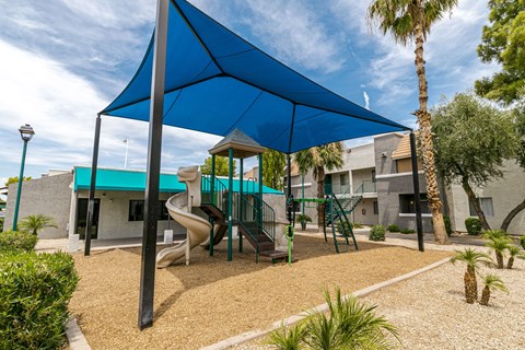 A playground with a blue shade structure and a slide.