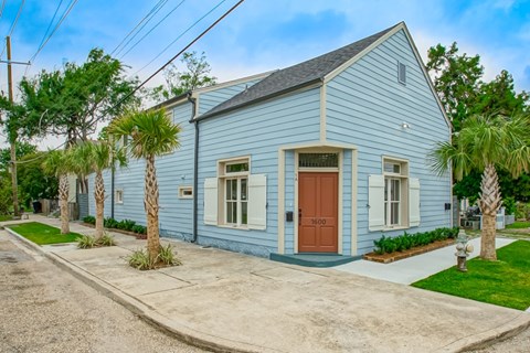 A blue house with a brown door and windows surrounded by greenery.