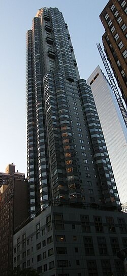 A tall building with many windows stands in front of a building with a crane on it.