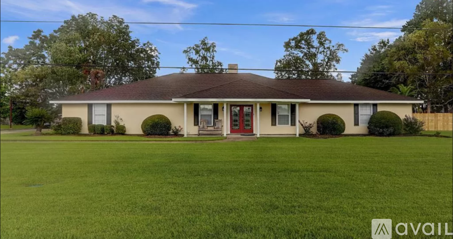 A house with a red door and a brown roof is surrounded by a green lawn.