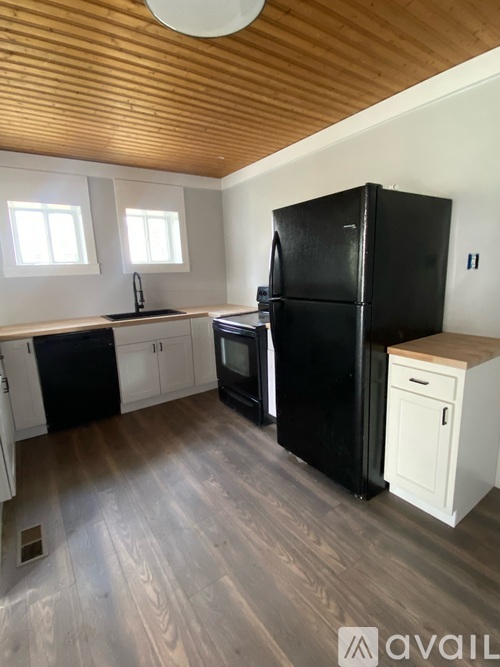 A kitchen with a black fridge and wooden floors.