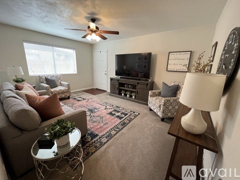 A living room with a grey couch, a rug, a white side table, a wooden end table, and a ceiling fan.