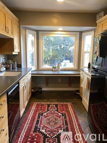 A kitchen with a rug on the floor and a window letting in light.