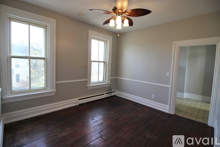 A room with a ceiling fan and two windows.