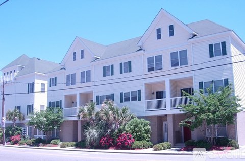 A white apartment building with balconies and trees in front.