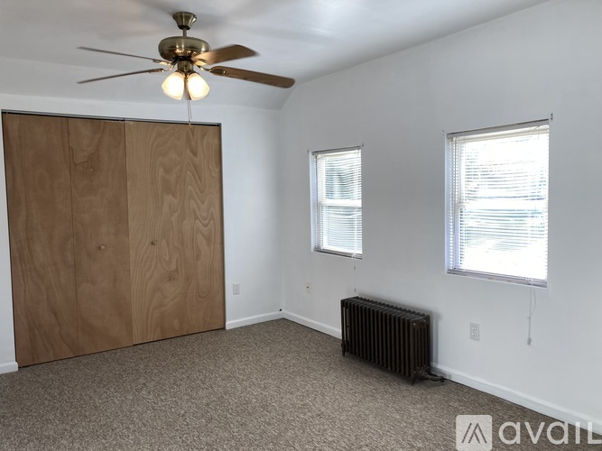 A room with a ceiling fan, two windows, and a radiator.
