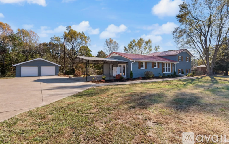 A house with a garage is situated in a grassy area with trees in the background.