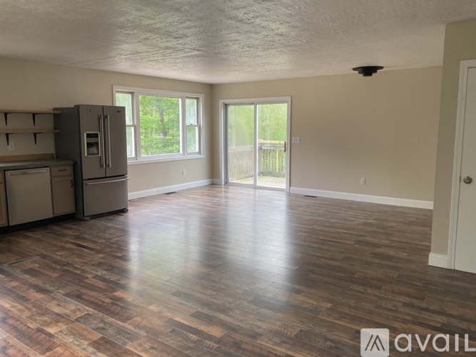 A spacious room with wooden flooring and a refrigerator in the corner.
