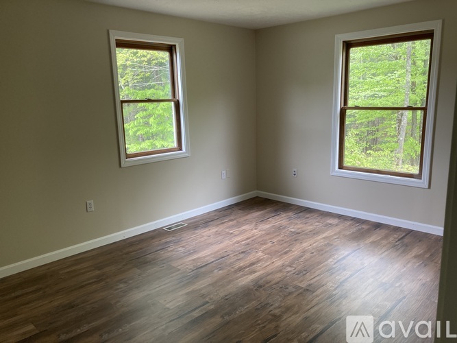 A room with wooden floors and two windows showing greenery outside.