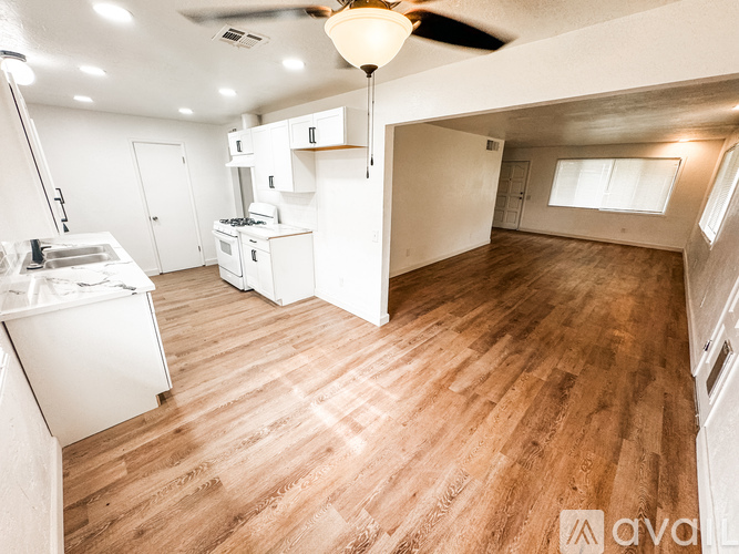 A well-lit kitchen and living room with wooden floors and white walls.