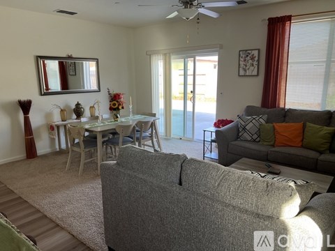 A living room with a grey couch and a dining table with chairs.