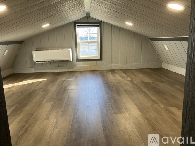 A spacious attic room with wooden flooring and a window.