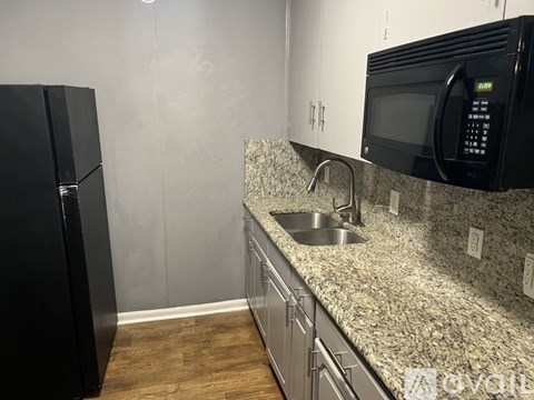 A black fridge and microwave in a kitchen with a granite countertop.