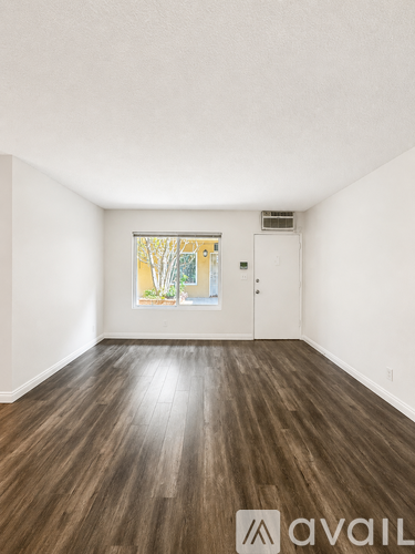A room with wooden floors and a window showing trees outside.
