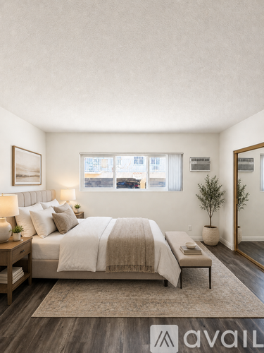 A bedroom with a large bed, a nightstand with a lamp, a bench, and a plant.