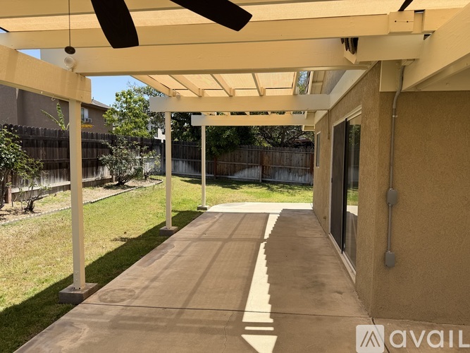 A patio with a white pergola and a ceiling fan.