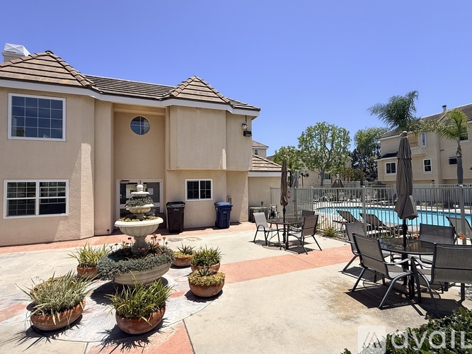 A poolside area with a fountain, chairs, and a building in the background.