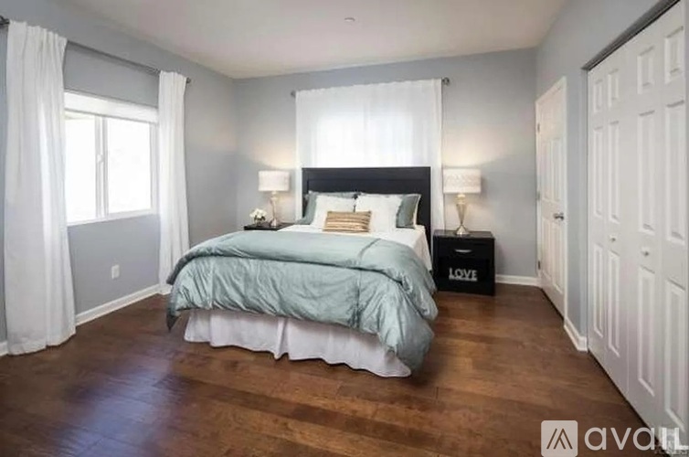 A bedroom with a bed, nightstand, and a window with white curtains.