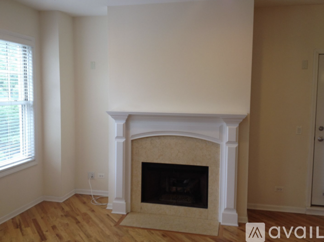 A fireplace with a beige mantle and a white frame is in a room with wooden floors and white walls.