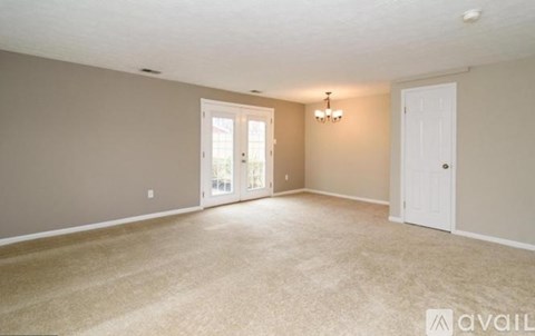 A spacious room with beige carpeting and a chandelier.
