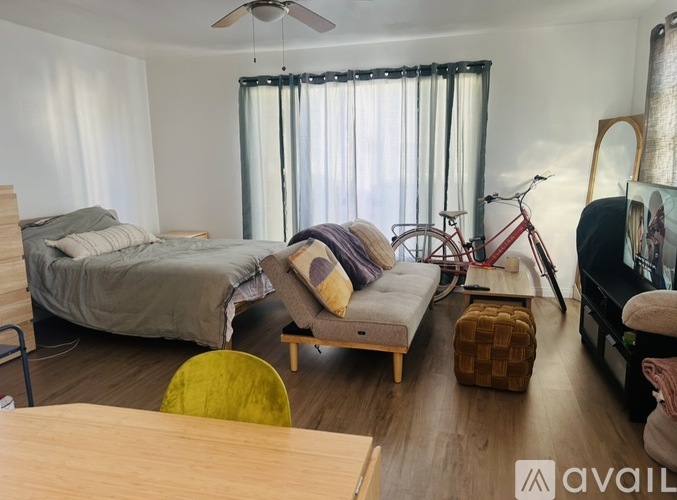 A bedroom with a bed, a couch, a chair, a bicycle, and a ceiling fan.