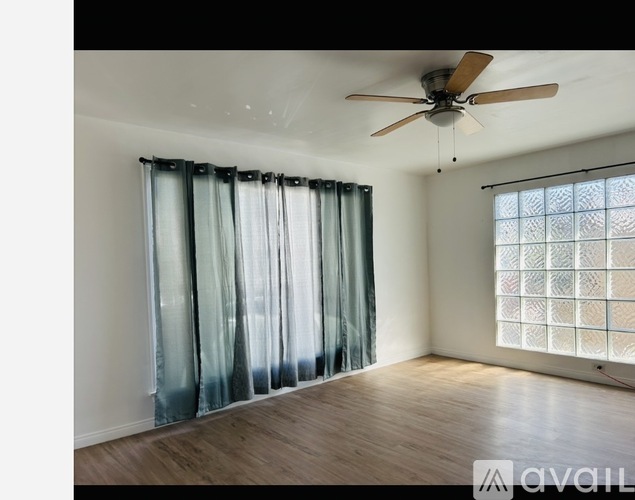 A room with a ceiling fan and a window with a curtain.