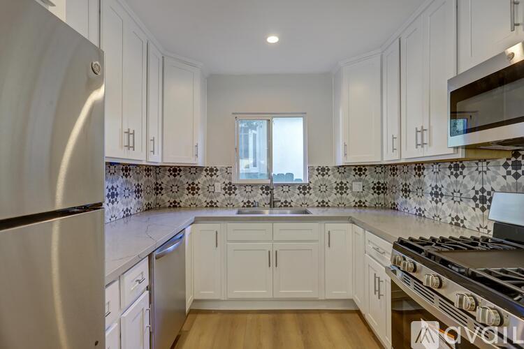 A kitchen with white cabinets and a black and white tiled backsplash.