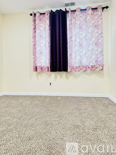 A room with a carpet and a window with curtains.
