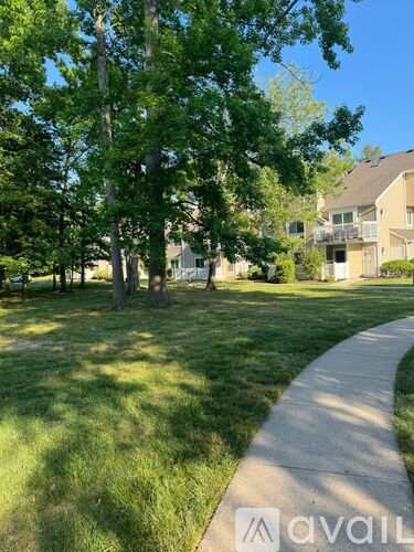 A grassy area with a sidewalk and trees in front of a building.