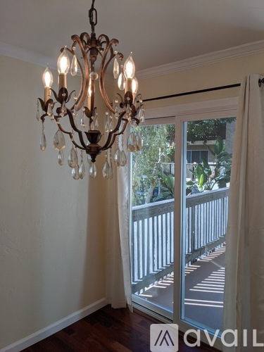 A chandelier hangs in a room with a sliding glass door leading to a balcony.