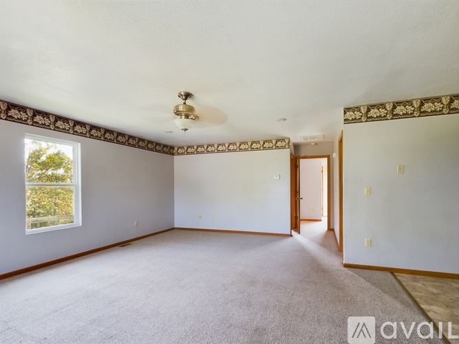 A spacious room with a carpeted floor and a window showing greenery outside.
