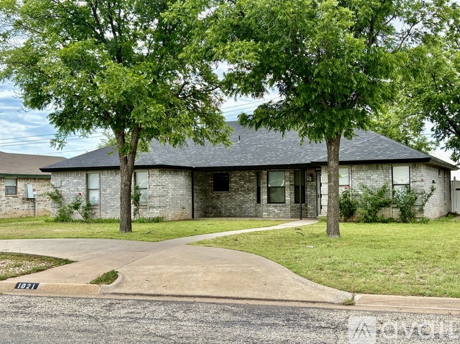 A house with a driveway and two trees in front.