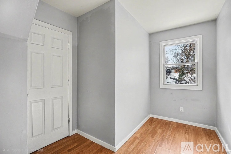 A room with a white door and a window with a view of trees and a house.